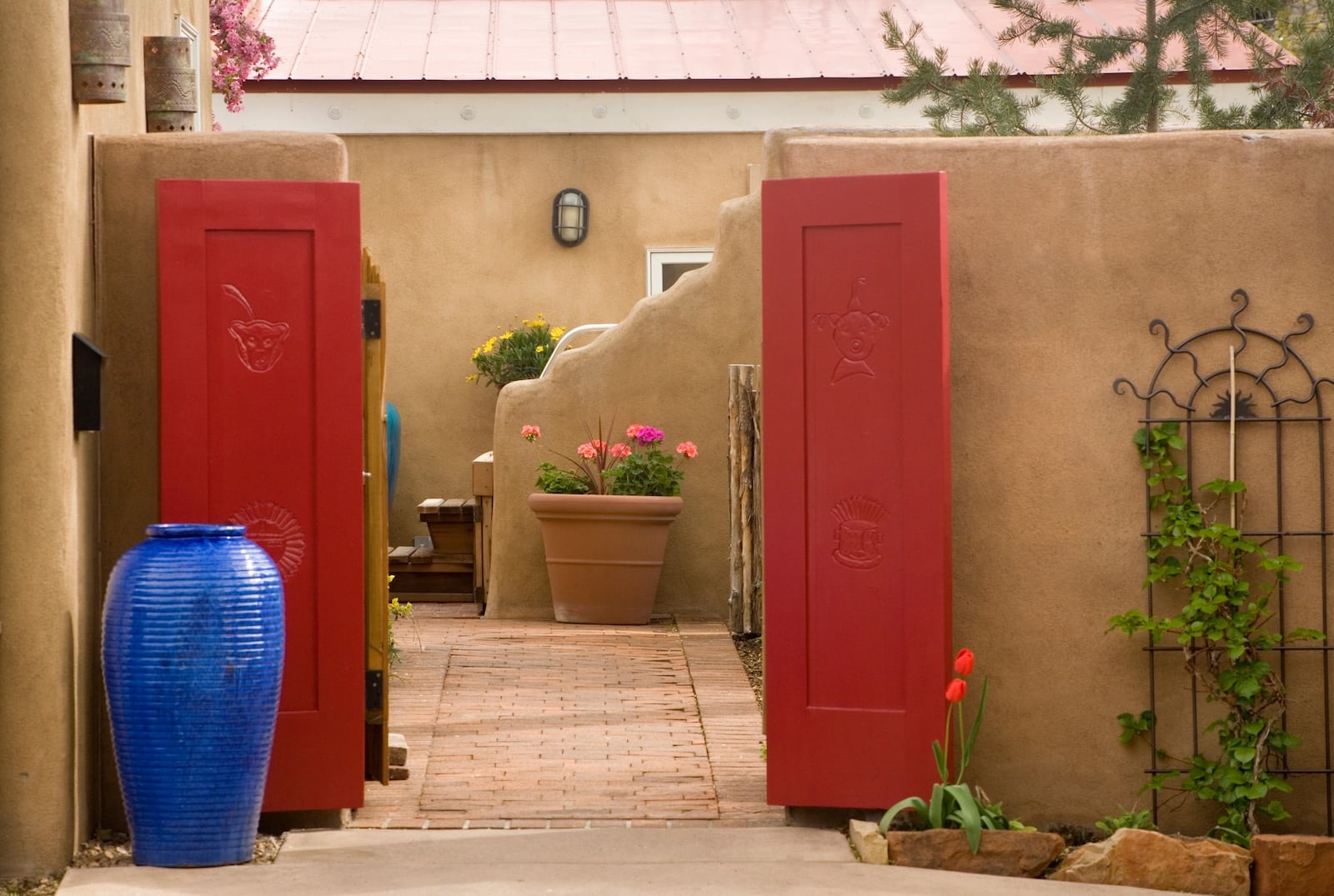 A patio with red doors, blue pots, and clay pots filled with flowers at a Santa Fe Bed and Breakfast. 