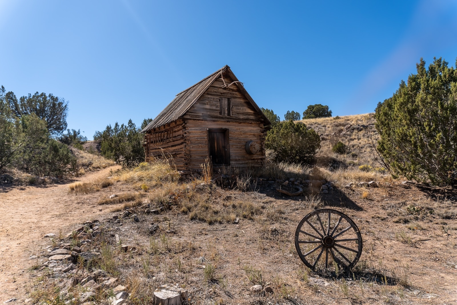 A small cabin on land with a wheel in front of it at El Rancho de las Golondrinas.