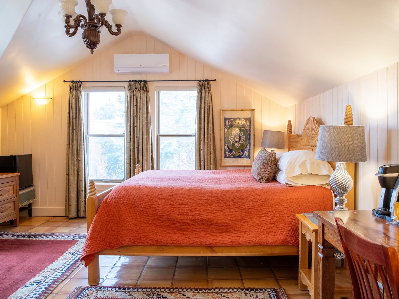 This room at Four Kachinas, the Santa Fe best bed and breakfast, features a bed with an orange comforter by two windows. 